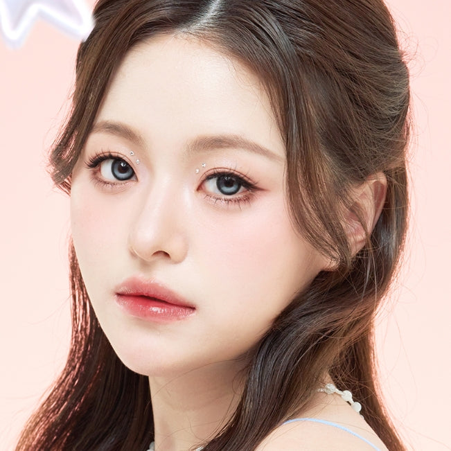 A close-up portrait of a young woman with long dark brown hair, wearing a light blue top against a soft pink background.