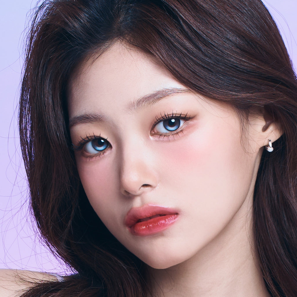 Close-up of a person with long dark hair and blue eyes against a light purple background